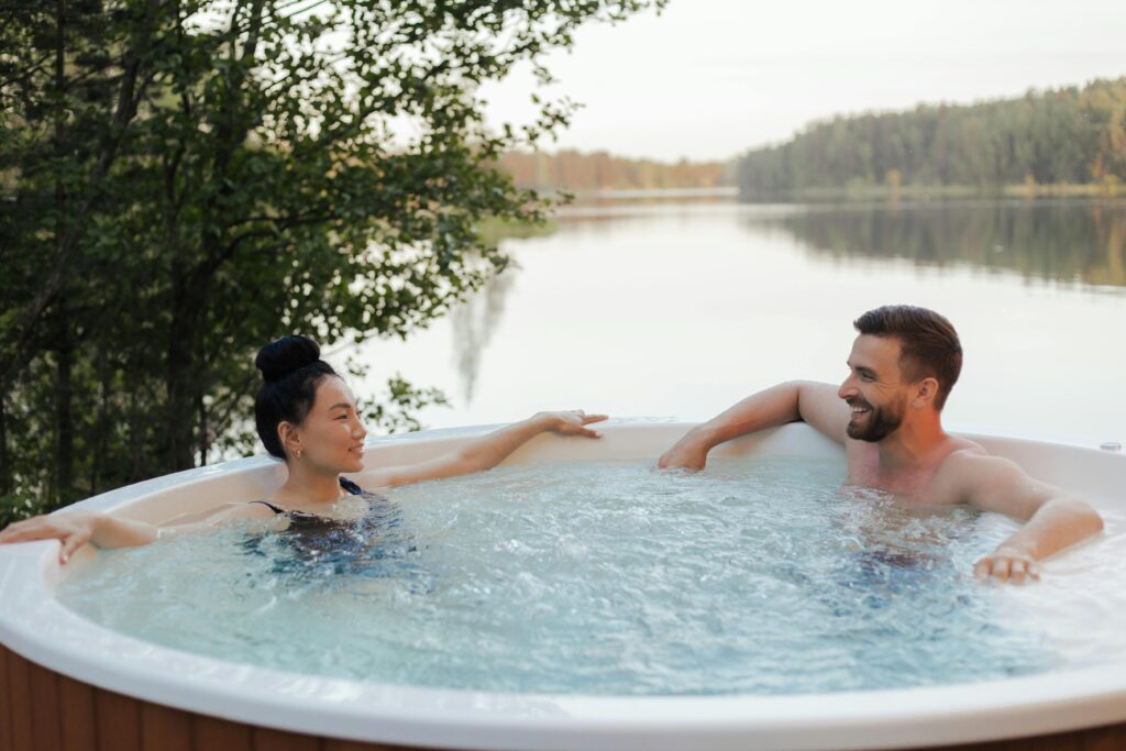 Couple enjoying a relaxing moment in an outdoor jacuzzi by a scenic lake at sunset.