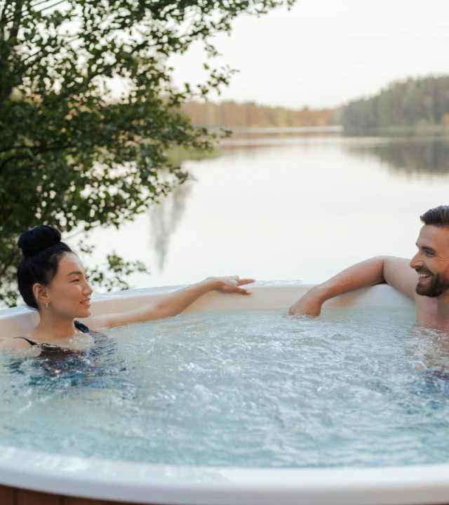 Couple enjoying a relaxing moment in an outdoor jacuzzi by a scenic lake at sunset.
